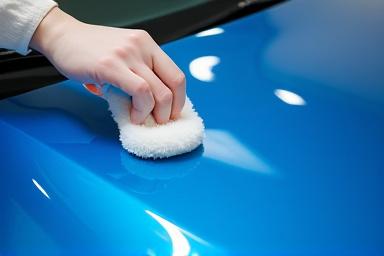 Mano aplicando capa cerámica a un capó de coche azul.